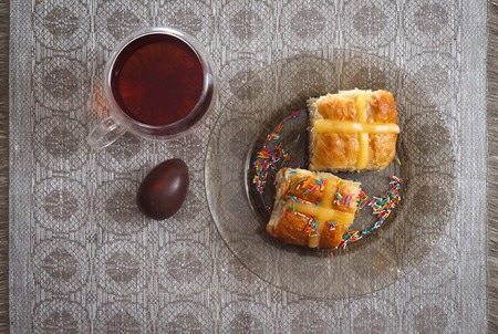 Hot cross buns, cup of tea and chocolate eggs on easter breakfast table, horizontal top view