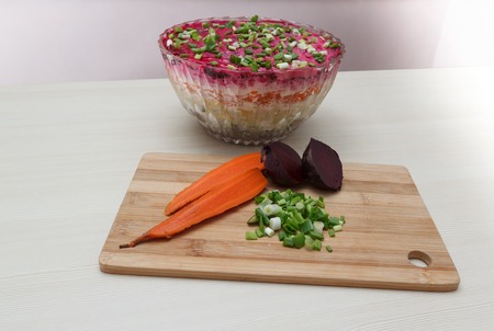 Traditional Russian herring salad in a transparent glass bowl with ingredients on a wooden cutting board, horizontal viewの写真素材