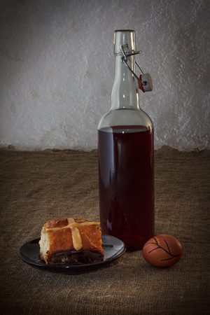 Easter dinner served on burlap tablecloth. Bottle of wine, hot cross bun, and egg.の写真素材
