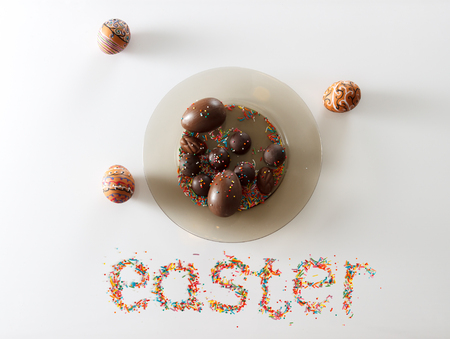 Easter made from raisins and colorful baking sugar over white background with a plate full of chocolate eggs and candies and two hand drawn eggs, horizontal top viewの写真素材