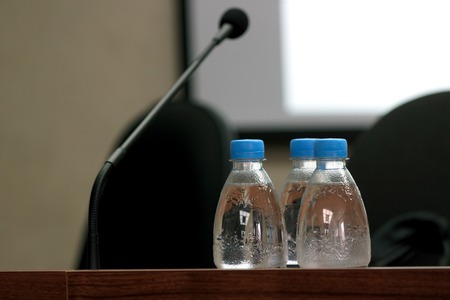 Seminar podium with blank screen, microphone and bottles of water on table ready for the speaker, selective focus, horizontal viewの写真素材