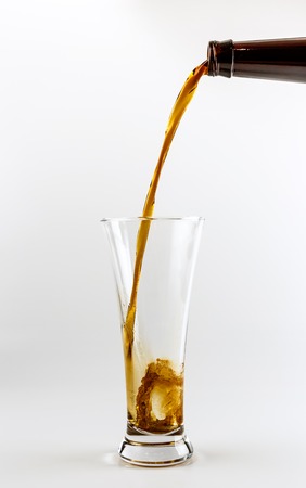 Pouring process of lager beer into a beer glass, splashes, drops and froth around glass against white backgroundの写真素材