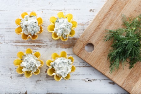 Tartlets filled with cheese and dill salad against rustic wooden background with cutting board by side, horizontal top  viewの写真素材