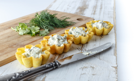 Tartlets filled with cheese and dill salad against rustic wooden background with knife and cutting board by side, close up, horizontal view, shallow DOFの写真素材
