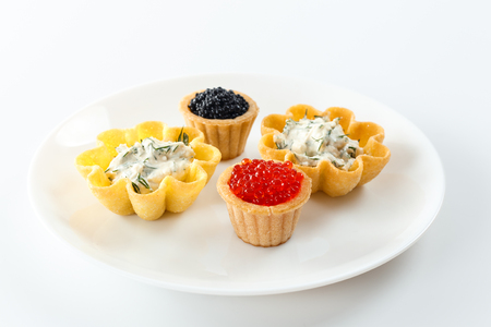 Tartlets filled with red and black caviar and cheese and dill salad on white plate against white background, close up, horizontal view with shallow DOFの写真素材