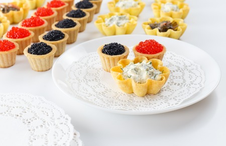 Tartlets filled with cheese and dill salad and caviar and plate with tartlets against white background, close up, horizontal viewの写真素材
