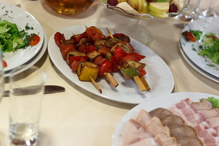 Grilled vegetables skewers and various sliced meat on plate on banquet table, overhead view selective focusの写真素材