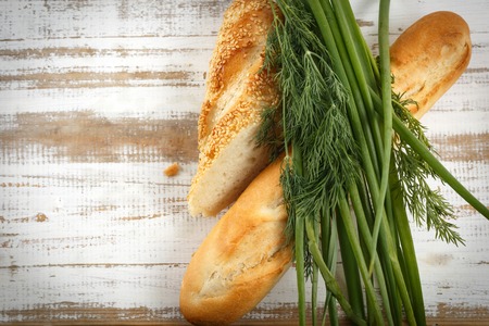 Crusty fresh seasoned baguette with sesame with fresh herbs on rustic wooden background, horizontal top view with copy spaceの写真素材