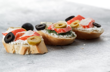Tasty various italian sandwiches with seafood against rustic wooden background. Crostini with cheese, crab sticksand sliced olives, horizontal view, close up with selective focusの写真素材