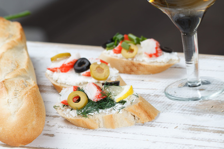 Tasty various italian sandwiches with seafood against rustic wooden background. Crostini with cheese, crab sticks and olives, bread and wine, close up, horizontal view with selective focusの写真素材
