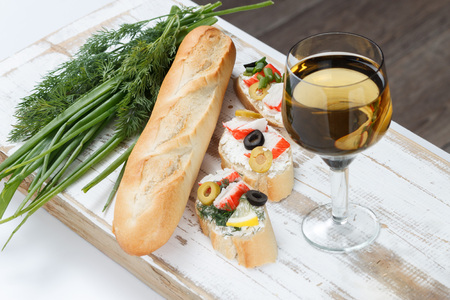 Tasty various italian sandwiches with seafood against rustic wooden background. Crostini with cheese, crab sticks and olives, bread, herbs and wine, close up with selective focusの写真素材