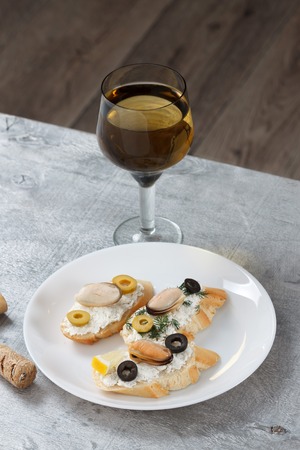 Tasty various italian sandwiches with seafood against rustic wooden background. Crostini with cheese, mussels and olives on white plate and wine, close up with selective focusの写真素材