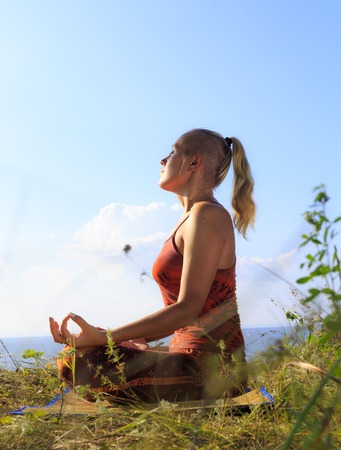 Beautiful young woman practising yoga on mat outdoors at river bank on grass, close upの写真素材