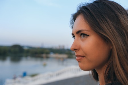 Young beautiful woman portrait against sunset in park and city at background, horizontal view
