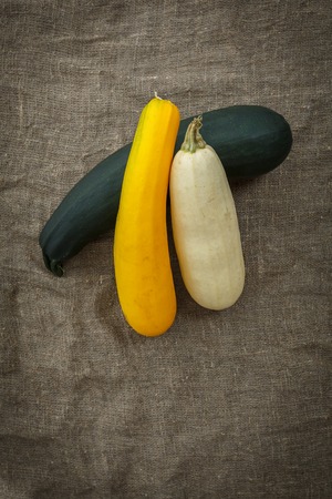 Fresh zucchini or marrow squash or courgette on rustic burlap background. Vegetables in different shapes and colors, concept of diversity, top viewの写真素材