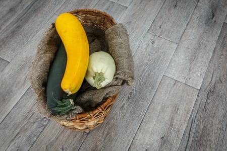 Fresh zucchini or marrow squash or courgette in basket on burlap against wooden background. Vegetables in different shapes and colors, concept of diversity, top view with copy spaceの写真素材
