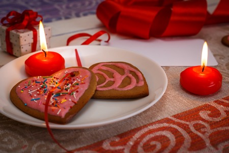 Chocolate gingerbread cookies heart shaped with pink icing and red ribbon, heat shaped candles and gift box on colorful fabric with card with copy space, selective focus, Valenite's day conceptの写真素材