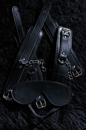 Low key photo of shiny leather cuffs for hands and legs and blinfold for erotic games against furの写真素材