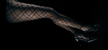 Low key photo of sexy slim beautiful legs in black net tights and high heel shoes lying on fur against black background, horizontal viewの写真素材