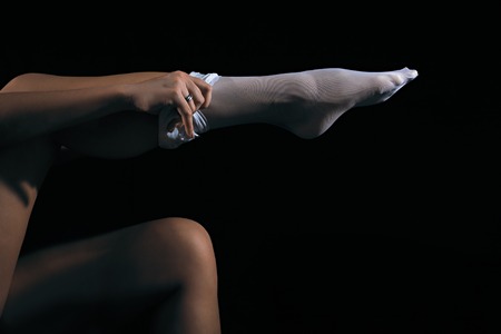 Low key photo of sexy woman put on her white nylon stockings on long fit legs against dark background, horizontal viewの写真素材