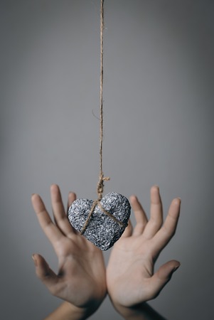 Hands holding a stone heart in jute bondage against grey background, Valentine's day concept