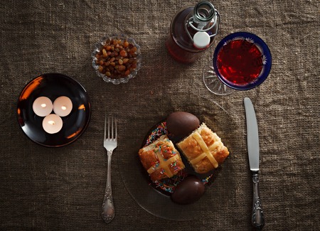 Easter dinner served on burlap tablecloth. Meat, hot cross buns, chocolate eggs and wine, horizontal...