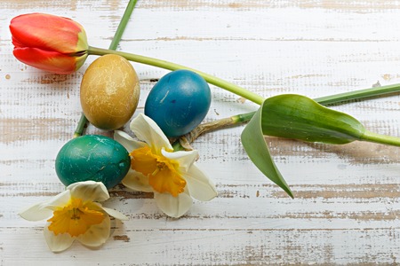 Bouquet of red spring tulip, daffodils and handmade colorful painted easter eggs against rustic wooden background, close up horizontal top view. Easter greeting cardの写真素材