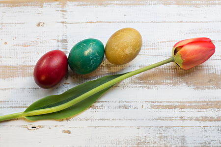 Bouquet of red spring tulip and handmade colorful painted easter eggs against rustic wooden background, close up horizontal top view. Easter greeting cardの写真素材
