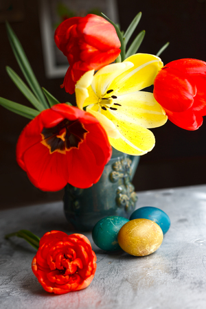 Bouquet of red and yellow spring tulips and handmade colorful painted easter eggs against rustic wooden background, close up selective focus. Easter greeting cardの写真素材