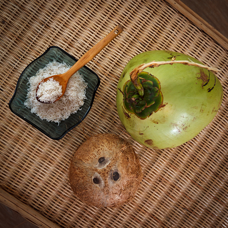 young and old coconuts with bowl full of coconut flakes on table top viewの写真素材