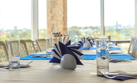 Empty half-served banquet table in restaurant with napkins, glasses, forks, knives, shallow DOF view against blurred city skyline background Empty half-served banquet table in restaurant with napkins, glasses, forks, knives, shallow DOF view against blurred city skylineの写真素材