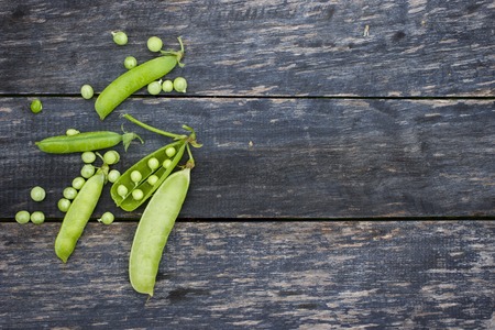 Pods of green peas and pea on a dark wooden surface, top view