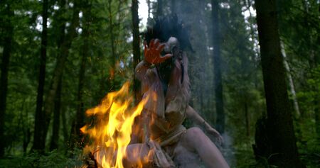 mystic lady in mask moves hands above bright orange bonfireの写真素材