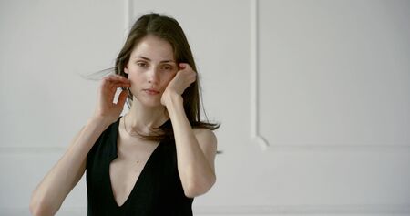 young slender woman is touching her hair and looking at camera, posing in studio