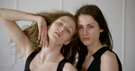portrait of two girls models close-up. One is light and one is dark. They pose in a bright Studio. Their hair flutters in the wind.の写真素材