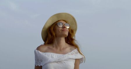 charming redhead woman is walking alone in summer day, tilt up view against blue skyの写真素材
