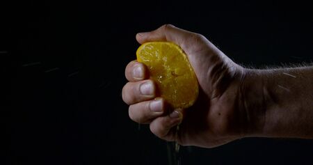 male hand is squeezing a half of ripe orange, close-ip on black background