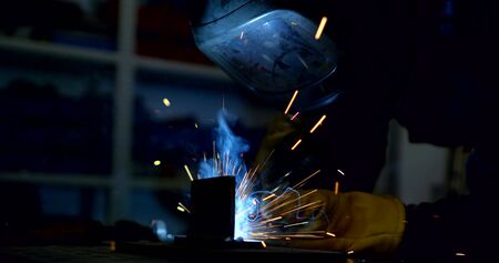 worker in mask welds details with sparks and smoke in shop