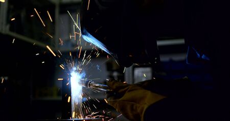 employee in welding mask connects details with modern tool
