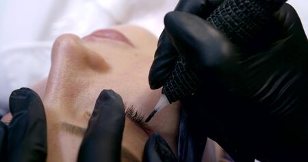 beautician applies make-up on eyelid with special ink gunの写真素材