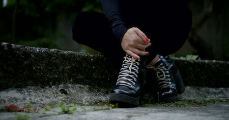 closeup view of crossed legs and hands of young woman sitting on footway in cityの写真素材