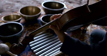 Close - up of a blonde woman sitting on a stone surface and conducts sound therapy, massage sound vibrations, playing the violin, standing around her bowl.の写真素材