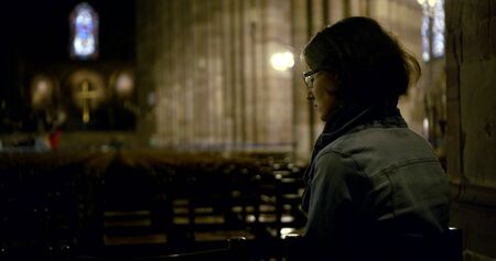 Portrait dark-haired woman of middle age, on her face she has glasses, she sits in a Catholic Cathedral on chairs. Rear view.の写真素材