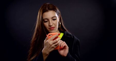 happy girl is typing message in smartphone, looks at camera and smiling broadlyの写真素材
