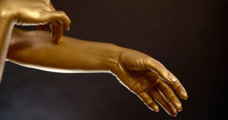 Close-up portrait of women's hands in gold pigment on a black background in the Studio. They make dancing movements.の写真素材