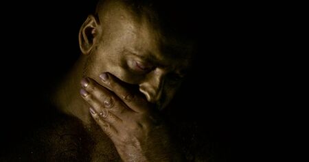 brawny adult man is covered bronze dye is standing in darkness