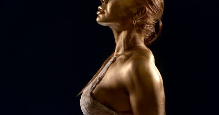 the body, back fit athletic girl bodybuilder in a shiny bikini, she is in the Studio on a black background, she has a Golden pigment on her skin, a ponytail is tied on her head. Shes posing.の写真素材