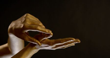 Close-up portrait of women's hands in gold pigment on a black background in the Studio. They make stroking movements.の写真素材