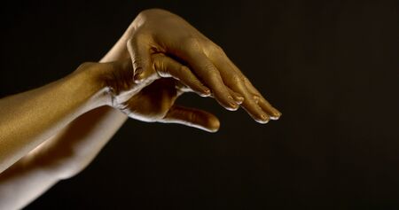 Close-up portrait of women's hands in gold pigment on a black background in the Studio. They make stroking movements.の写真素材