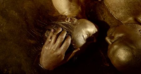 portrait of a passionate naked couple: a bald man and a dark-haired woman, their whole body in gold pigment, skin glistening, they lie in a pool of Golden water, hugging, gently stroking each other.の写真素材